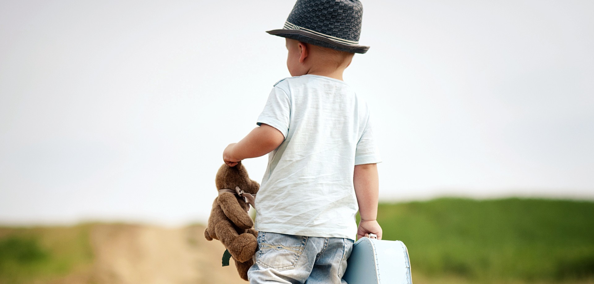 Foto eines Jungen, der mit einem Koffer und Teddybär einen Weg entlang geht (Bild: AdobeStock/Halfpoint).