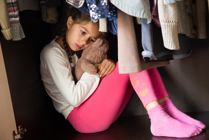 Mädchen sitzt ängstlich und gekrümmt in einem Kleiderschrank (zabavna - stock.adobe.com)