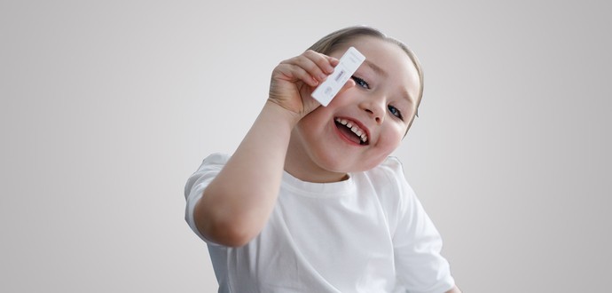 Kind hält lächelnd einen negativen Covid-Schnelltest in der Hand (Foto: Alena Stalmashonack – stock.adobe.com)