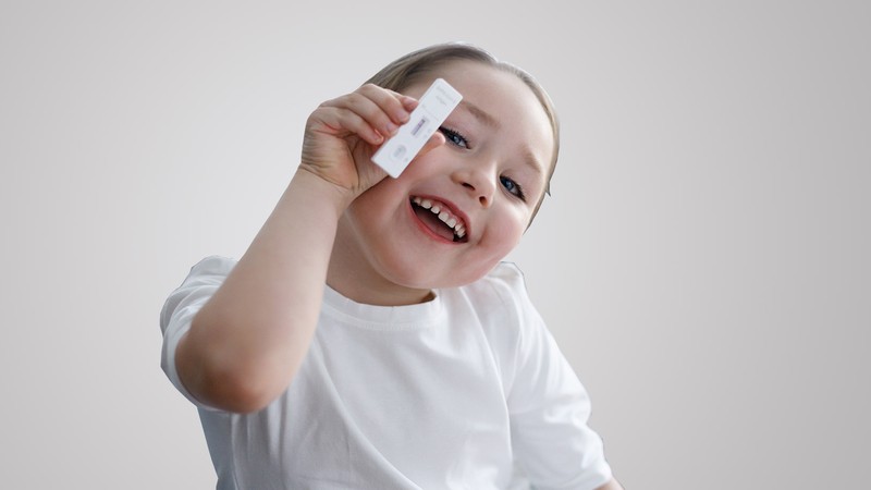 Kind hält lächelnd einen negativen Covid-Schnelltest in der Hand (Foto: Alena Stalmashonack – stock.adobe.com)