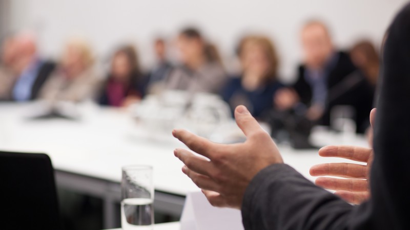 Seminarsituation mit einer vortragenden Person und Personen im Hintergrund