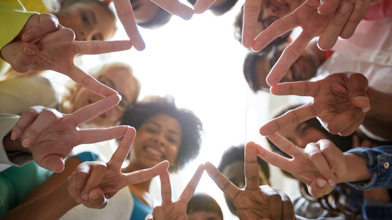 Junge Menschen unterschiedlicher Nationen im Kreis zeigen mit ihren Händen Friedenszeichen